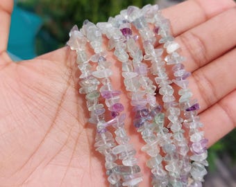 May include: A strand of multi-colored fluorite chip beads featuring translucent shades of pale green, clear white, and vibrant purple. The small, irregular, polished stone fragments are strung together to form a continuous, textured necklace.