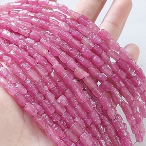 Puede incluir: Una hebra de cuentas de piedras preciosas rosadas, facetadas y talladas en bruto. Las cuentas son de forma rectangular y tienen un aspecto ligeramente irregular y natural.