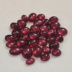 May include: A collection of oval-shaped, red gemstones. The gemstones are smooth and polished, with a glossy finish.