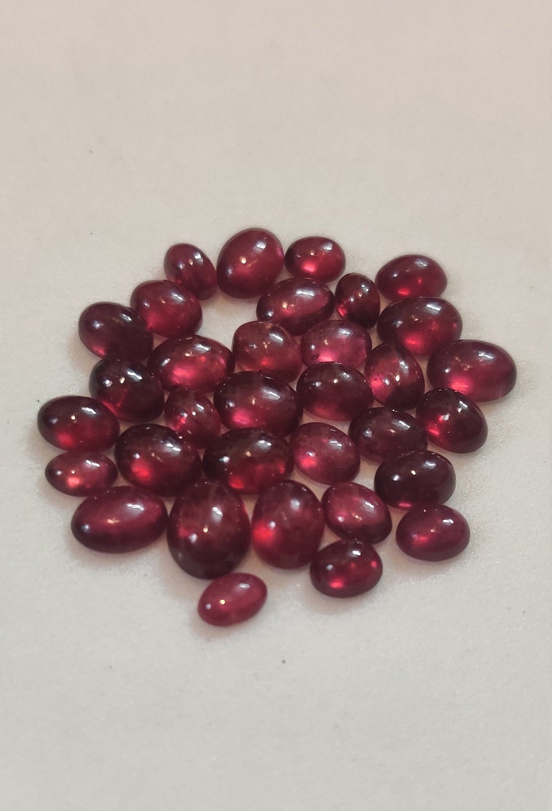 May include: A collection of oval-shaped, red gemstones. The gemstones are smooth and polished, with a glossy finish.