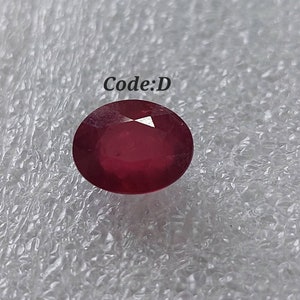 Puede incluir: Una piedra preciosa ovalada de color rojo intenso con un corte facetado. La piedra preciosa está sobre un fondo blanco con el texto "Code:D" encima.