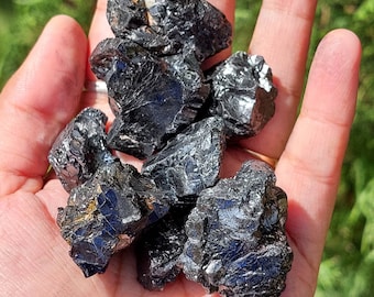 Könnte beinhalten: Eine Sammlung schwarzer, rauer und unregelmäßig geformter Kristalle. Die Kristalle haben ein glänzendes, fast metallisches Aussehen.