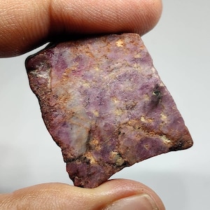 Peut inclure: Une pierre précieuse brute de couleur violette et brune avec une apparence marbrée. La pierre est de forme irrégulière et a une finition naturelle non polie.
