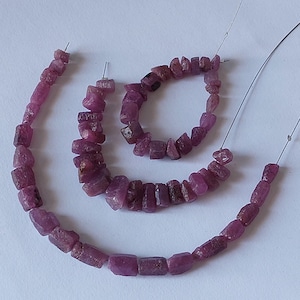 May include: Strands of rough-cut, deep pink ruby gemstone beads. The beads are strung on thin wire, ready for jewelry making. The gemstones have a natural, irregular shape and a slightly translucent appearance. The beads are arranged in a spiral pattern.