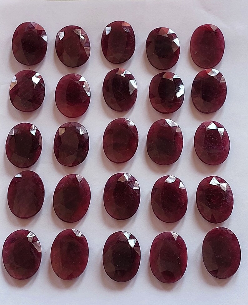 Puede incluir: Veinticuatro piedras preciosas ovaladas de color rojo oscuro dispuestas en cuatro filas de seis. Las piedras preciosas son lisas y pulidas.