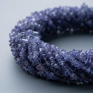 Op de afbeelding: Een cirkelvormige armband opgebouwd uit talloze kleine, onregelmatige, getrommelde tanzaniet edelsteensplinters. De diep violetblauwe stenen zijn dicht op elkaar gepakt, wat zorgt voor een textuurrijk, meerlagig uiterlijk met een egale kleur.