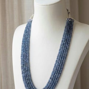 Puede incluir: Un collar de múltiples hilos que presenta numerosas cuentas pequeñas de piedras preciosas azules facetadas dispuestas en varias capas en cascada. Los hilos se reúnen en la parte superior con detalles de metal plateado, creando un aspecto uniforme.