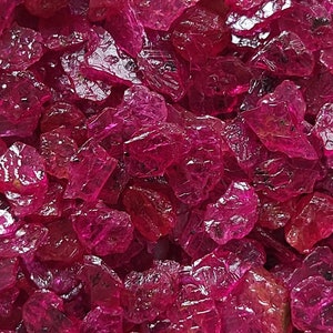 Op de afbeelding: Een close-up van een stapel roze robijn edelstenen. De ruwe, ongeslepen stenen hebben verschillende vormen en maten, en ze zijn allemaal erg glanzend.