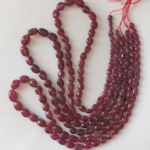 May include: A strand of oval-shaped, deep red gemstone beads. The beads are strung on a thin cord and are approximately 10mm in length. The beads are arranged in a loose, flowing pattern.