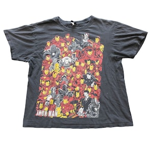 Op de afbeelding: Donkergrijs t-shirt met een afbeelding van Iron Man-personages in rood, geel en grijs. Het ontwerp toont verschillende poses en pantserontwerpen. De tekst "Iron Man" staat onderaan. Ronde hals.