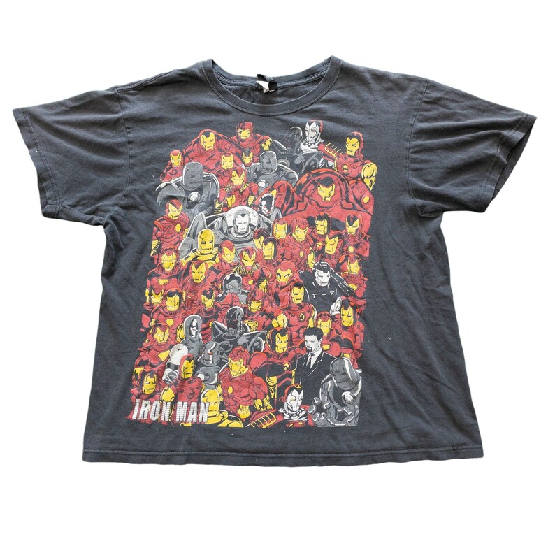 Op de afbeelding: Donkergrijs t-shirt met een afbeelding van Iron Man-personages in rood, geel en grijs. Het ontwerp toont verschillende poses en pantserontwerpen. De tekst "Iron Man" staat onderaan. Ronde hals.