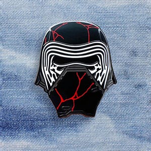 Może przedstawiać: Czarno-biała szpilka emaliowana z hełmem Kylo Rena z Gwiezdnych Wojen. Hełm ma czerwone pęknięcia na powierzchni.