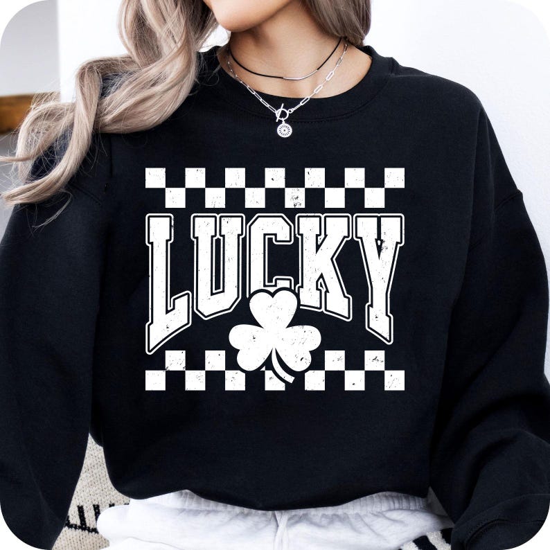May include: Black sweatshirt with the word "LUCKY" in white block letters, a white shamrock, and a checkered pattern. The sweatshirt is a crew neck style.