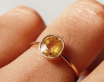 Puede incluir: Un anillo de oro con una piedra preciosa amarilla. El anillo está en el dedo de una persona.