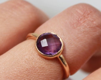 May include: A gold ring with a round, faceted amethyst gemstone.