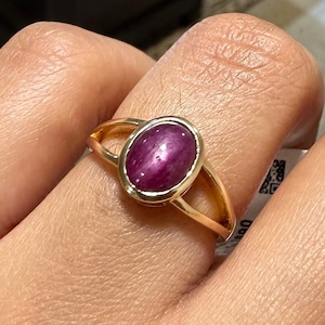 Op de afbeelding: Een gouden ring met een rode ovale robijn. De ring heeft een gespleten band.