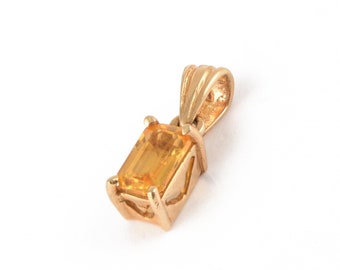 Op de afbeelding: Een gouden hanger met een gele edelsteen. De edelsteen is in een rechthoekige vorm geslepen.