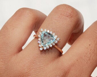 May include: A gold ring with a triangular aquamarine gemstone surrounded by a halo of smaller diamonds.