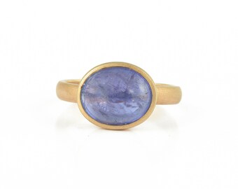 May include: A gold ring with a purple gemstone set in a bezel setting.