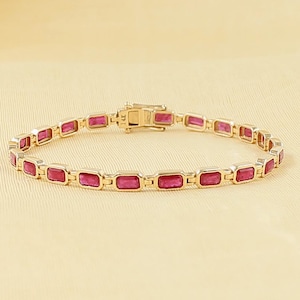 May include: A gold chain bracelet featuring a series of rectangular, vibrant pink gemstones set in individual metal frames. The bracelet is connected by small, polished gold links and includes a secure, rectangular clasp mechanism at the centre.