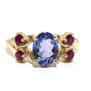 May include: A gold ring with a large oval blue gemstone surrounded by four smaller red gemstones.