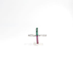 May include: A silver ring with a cross-shaped design. The ring features a row of green and red gemstones, with smaller white gemstones on the cross arms. The ring is set against a white background.