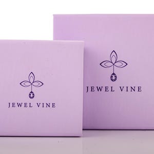 May include: Two light purple jewellery boxes of different sizes. Each box features a dark purple logo with a floral design and a gemstone pendant, along with the text "JEWEL VINE".