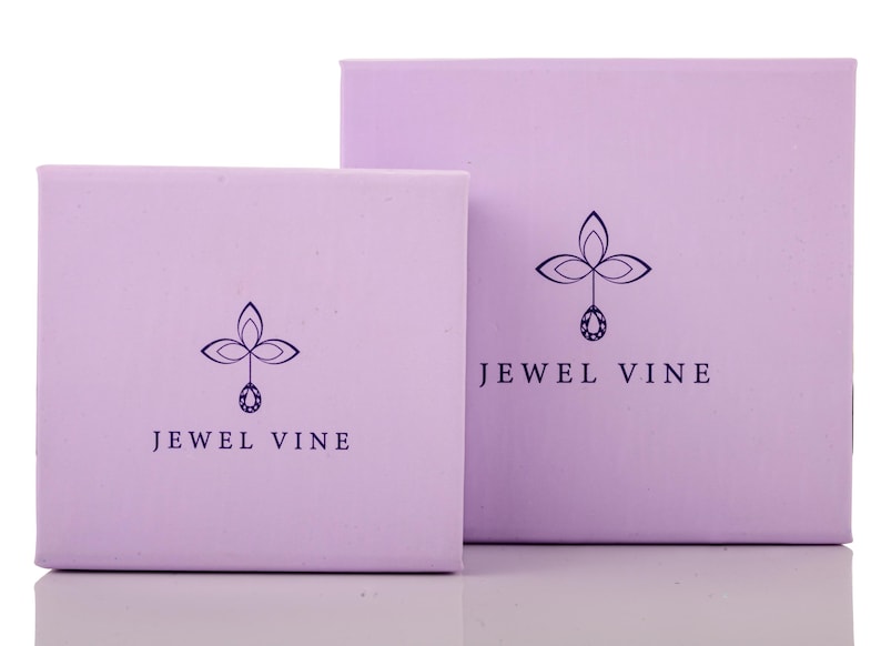 May include: Two light purple jewellery boxes of different sizes. Each box features a dark purple logo with a floral design and a gemstone pendant, along with the text "JEWEL VINE".