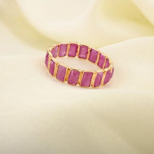 May include: A gold bracelet with pink rectangular gemstones. The bracelet is made of metal and has a simple design.