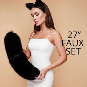Op de afbeelding: Een zwarte imitatiebontstaart, ongeveer 69 cm lang, vastgehouden door een persoon die een witte jurk draagt. De persoon draagt ook een zwarte kattenoren-hoofdband. De woorden "27" en "FAUX SET" zijn in zwart gedrukt.