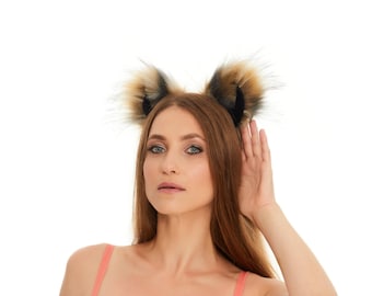 Può includere: Un cerchietto con due orecchie a punta e soffici in pelliccia sintetica nei toni del beige, marrone e nero. Le orecchie sono fissate a una fascia sottile e flessibile, progettata per essere indossata sul capo con un aspetto strutturato e multicolore.
