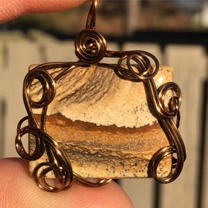 以下が含まれることがあります： 銅線で包まれたペンダントで、正方形の多色石には、茶色、白、黒の渦巻き模様が施されています。