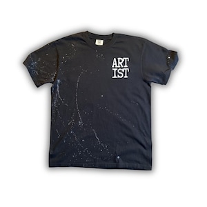 May include: Black t-shirt with white paint splatter design. The shirt features the text "ARTIST" in white block letters on the upper chest. A casual, artistic apparel item.