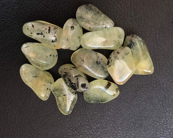 Puede incluir: Una colección de piedras de aventurina verde pulidas con inclusiones negras. Las piedras son lisas y pulidas, con una variedad de formas y tamaños.