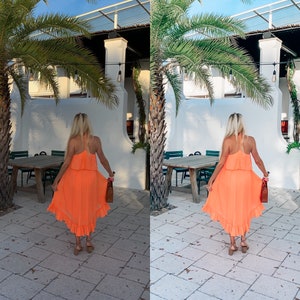 May include: A woman wearing a bright orange dress with a ruffled hem stands in front of a white building with palm trees. She is holding a brown handbag.