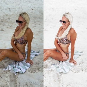 May include: A woman wearing a leopard print bikini top and matching bottoms sits on a white and blue striped towel on a sandy beach. She is wearing sunglasses and has blonde hair.