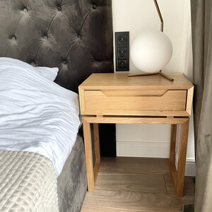 May include: A light wood nightstand with a single drawer and a white globe lamp on top. The nightstand has a simple, modern design and is made of solid wood.