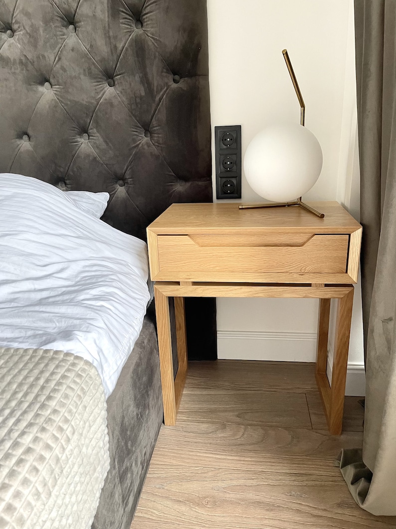 May include: A light wood nightstand with a single drawer and a white globe lamp on top. The nightstand has a simple, modern design and is made of solid wood.