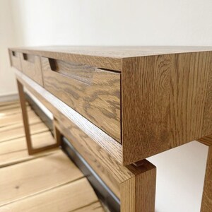 May include: A wooden console table with three drawers and a natural wood finish. The table has a simple, modern design and is supported by four legs.