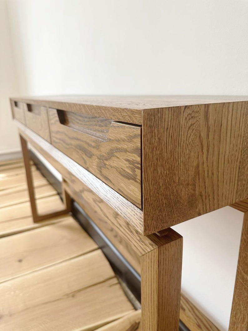 May include: A wooden console table with three drawers and a natural wood finish. The table has a simple, modern design and is supported by four legs.