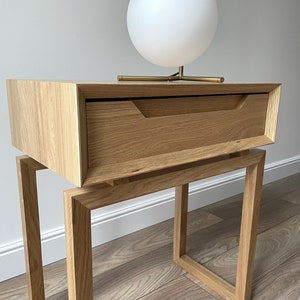 May include: A wooden bedside table with a single drawer and a square frame base. A white globe lamp sits on top of the table.