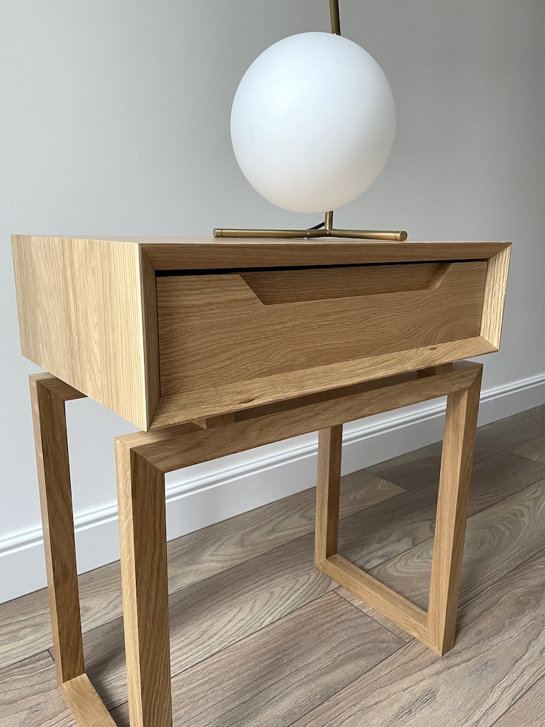 May include: A wooden bedside table with a single drawer and a square frame base. A white globe lamp sits on top of the table.
