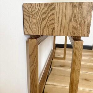 May include: A wooden table with a rectangular top and a simple, modern design. The table has a light brown finish and is made of solid wood. The table legs are made of the same wood and are rectangular in shape.