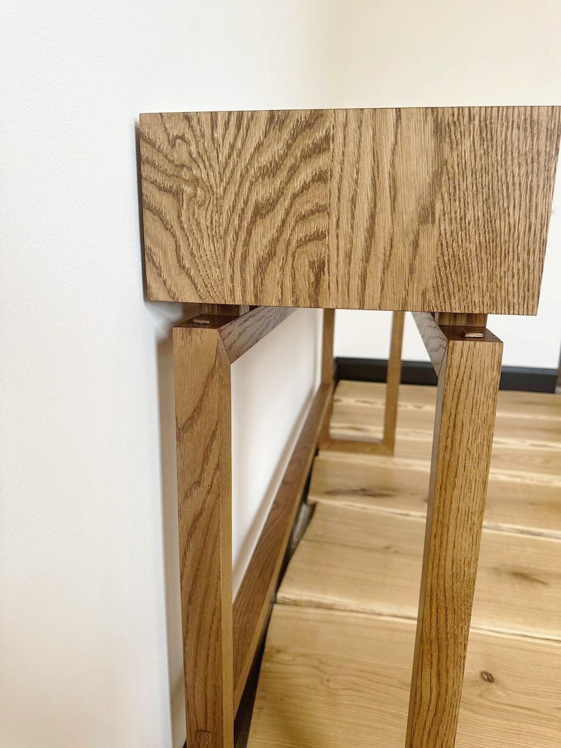 May include: A wooden table with a rectangular top and a simple, modern design. The table has a light brown finish and is made of solid wood. The table legs are made of the same wood and are rectangular in shape.