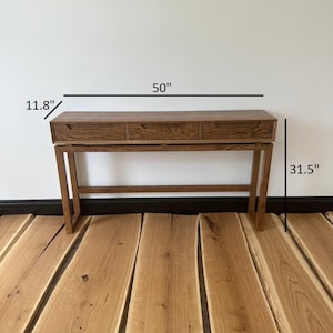 May include: A wooden console table with three drawers and a simple design. The table is 50 inches wide, 11.8 inches deep, and 31.5 inches tall.