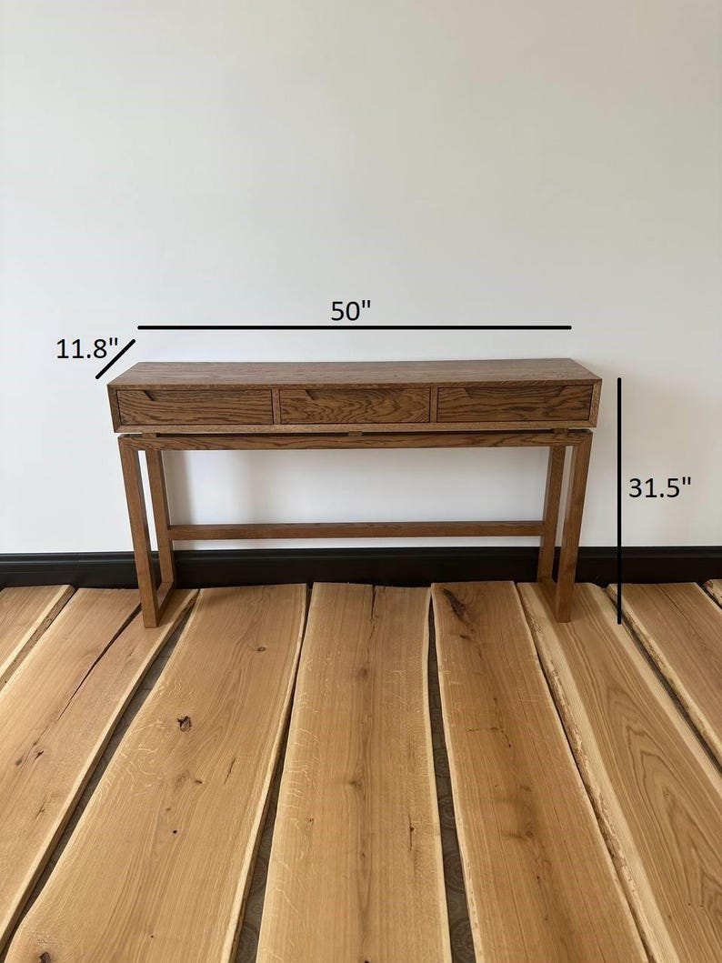 May include: A wooden console table with three drawers and a simple design. The table is 50 inches wide, 11.8 inches deep, and 31.5 inches tall.