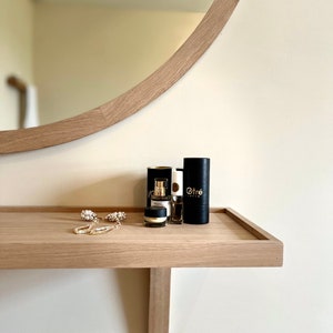 May include: A wooden shelf with a rounded mirror above it. The shelf has three small black bottles with gold lettering, two of which say "Otr&eacute;", and a pair of gold earrings.