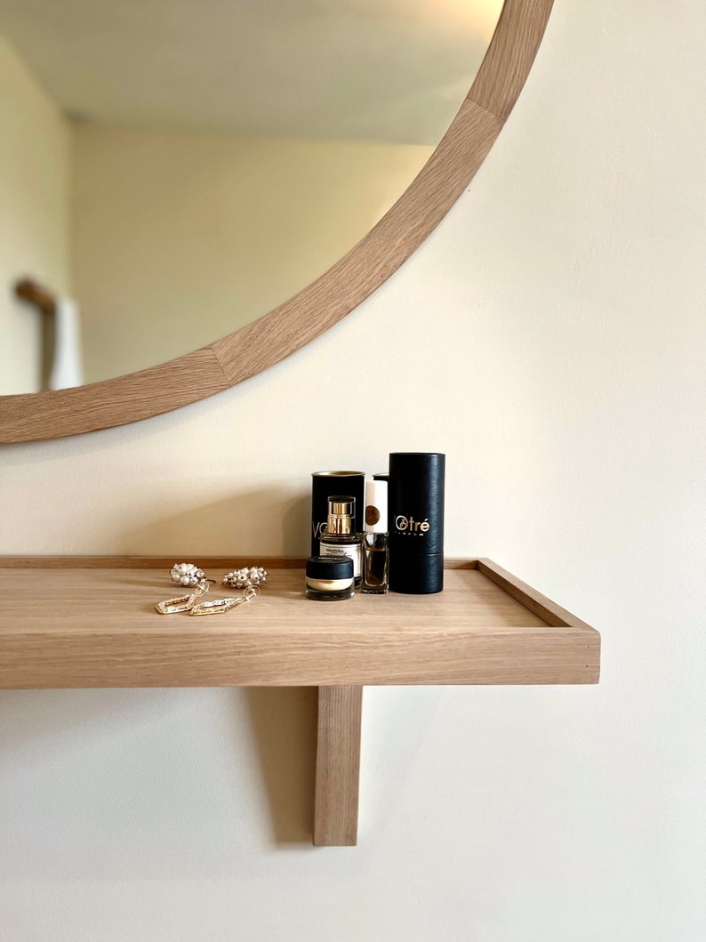 May include: A wooden shelf with a rounded mirror above it. The shelf has three small black bottles with gold lettering, two of which say "Otr&eacute;", and a pair of gold earrings.