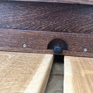 May include: Close-up of a wooden table with a black knob and two screws. The table is made of light brown wood with a grain pattern.