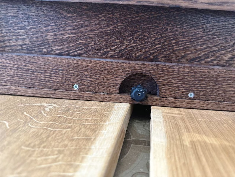 May include: Close-up of a wooden table with a black knob and two screws. The table is made of light brown wood with a grain pattern.